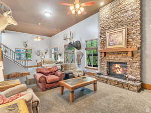 Carpeted living area featuring ceiling fan, a fireplace, stairs, and a towering ceiling