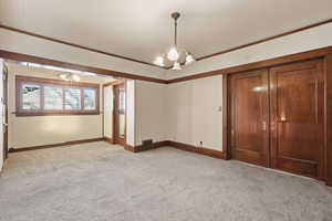Empty room with light colored carpet, a chandelier, and crown molding