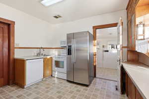 Kitchen featuring white appliances, light countertops, brown cabinetry, and light flooring