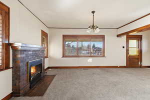 Unfurnished living room with carpet flooring, ornamental molding, a chandelier, and a fireplace