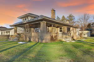 Back of property at dusk with a lawn, brick siding, and a chimney
