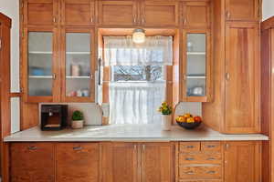 Bar with wood finish cabinetry, glass fronted cabinets, and light countertops