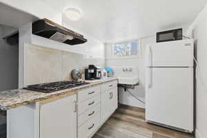 Kitchen featuring black appliances, light wood finished floors, ventilation hood, white cabinetry, and tasteful backsplash