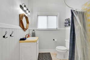 Bathroom featuring curtained shower, vanity, wainscoting, and light wood finished floors