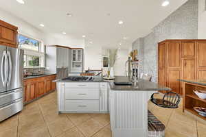 Dual tone kitchen with two tone color scheme, stainless steel appliances, dark stone countertops, brick wall, and a center island with sink