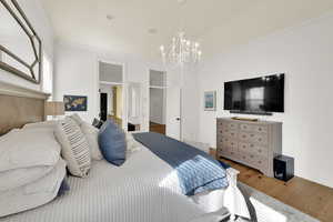 Bedroom featuring crown molding, wood finished floors, lofted ceiling, suspended lighting, and ensuite bathroom