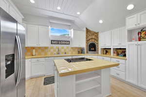 Kitchen with tile countertops, stainless steel refrigerator with ice dispenser, open shelves, white cabinets, and lofted ceiling