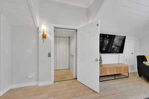 Corridor with crown molding, light wood-type flooring, and elevator
