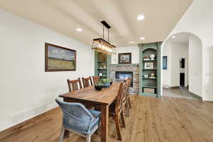 Dining area with a fireplace, light wood finished floors, arched walkways, built in features, and recessed lighting