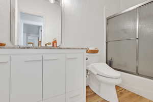 Bathroom featuring enclosed tub / shower combo, light wood finished floors, and vanity