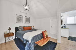 Bedroom with light wood finished floors, vaulted ceiling, and a chandelier