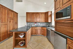 Kitchen featuring wood finish cabinetry, open shelves, dark stone counters, lofted ceiling, and stainless steel appliances