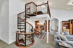 Staircase with a towering ceiling, recessed lighting, arched walkways, a stone fireplace, and carpet