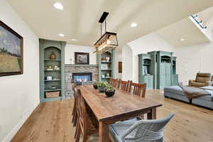 Dining area with light wood-style floors, a fireplace, vaulted ceiling, and recessed lighting