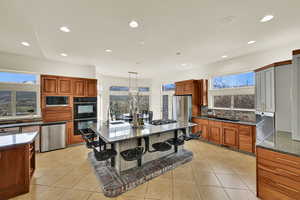 Kitchen featuring a kitchen bar, dark stone counters, stainless steel appliances, light tile patterned floors, and wood finish cabinetry