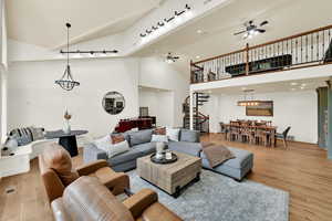 Living area featuring ceiling fan, light wood-type flooring, lofted ceiling, and a chandelier