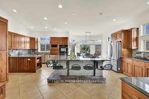 Kitchen with tasteful backsplash, a breakfast bar, wood finish cabinetry, stainless steel appliances, and dark stone countertops