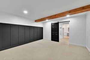 Basement featuring a barn door, light colored carpet, recessed lighting, and ornamental molding