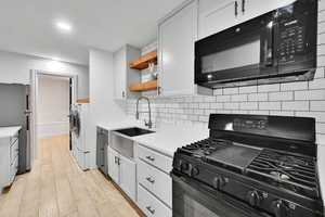 Kitchen with black appliances, open shelves, white cabinets, recessed lighting, and light wood finished floors
