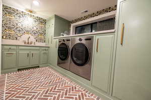 Laundry area with wallpapered walls, brick veneer flooring, cabinet space, and washing machine and clothes dryer