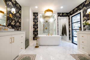 Primary bathroom featuring vanities, a chandelier, a freestanding bath, heated floors, recessed lighting, and wallpapered walls
