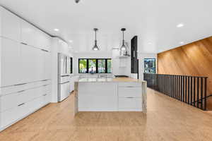 Kitchen with modern cabinets, white cabinetry, wood walls, light stone countertops, and decorative light fixtures