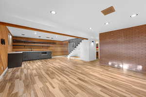 Unfurnished living room with brick wall, wood walls, light wood finished floors, stairway, and recessed lighting