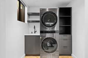 Laundry room with stacked washer and clothes dryer and light wood finished floors