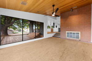 Unfurnished living room featuring wood ceiling, brick wall, a brick fireplace, plenty of natural light, and a ceiling fan