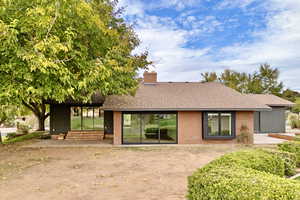Rear view of house featuring a patio, roof with shingles, a chimney, and brick siding