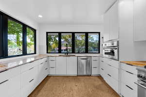 Kitchen with white cabinets, modern cabinets, stainless steel appliances, butcher block countertops, and recessed lighting