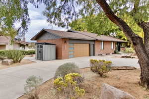 View of front of home featuring brick siding, driveway, an attached garage, and a chimney