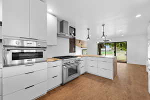 Kitchen with modern cabinets, white cabinetry, stainless steel appliances, light stone countertops, and wall chimney exhaust hood
