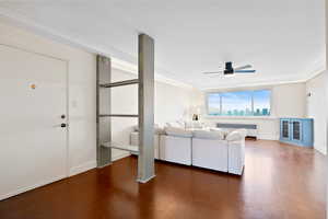 Living room with radiator heating unit, a ceiling fan, ornamental molding, and wood finished floors