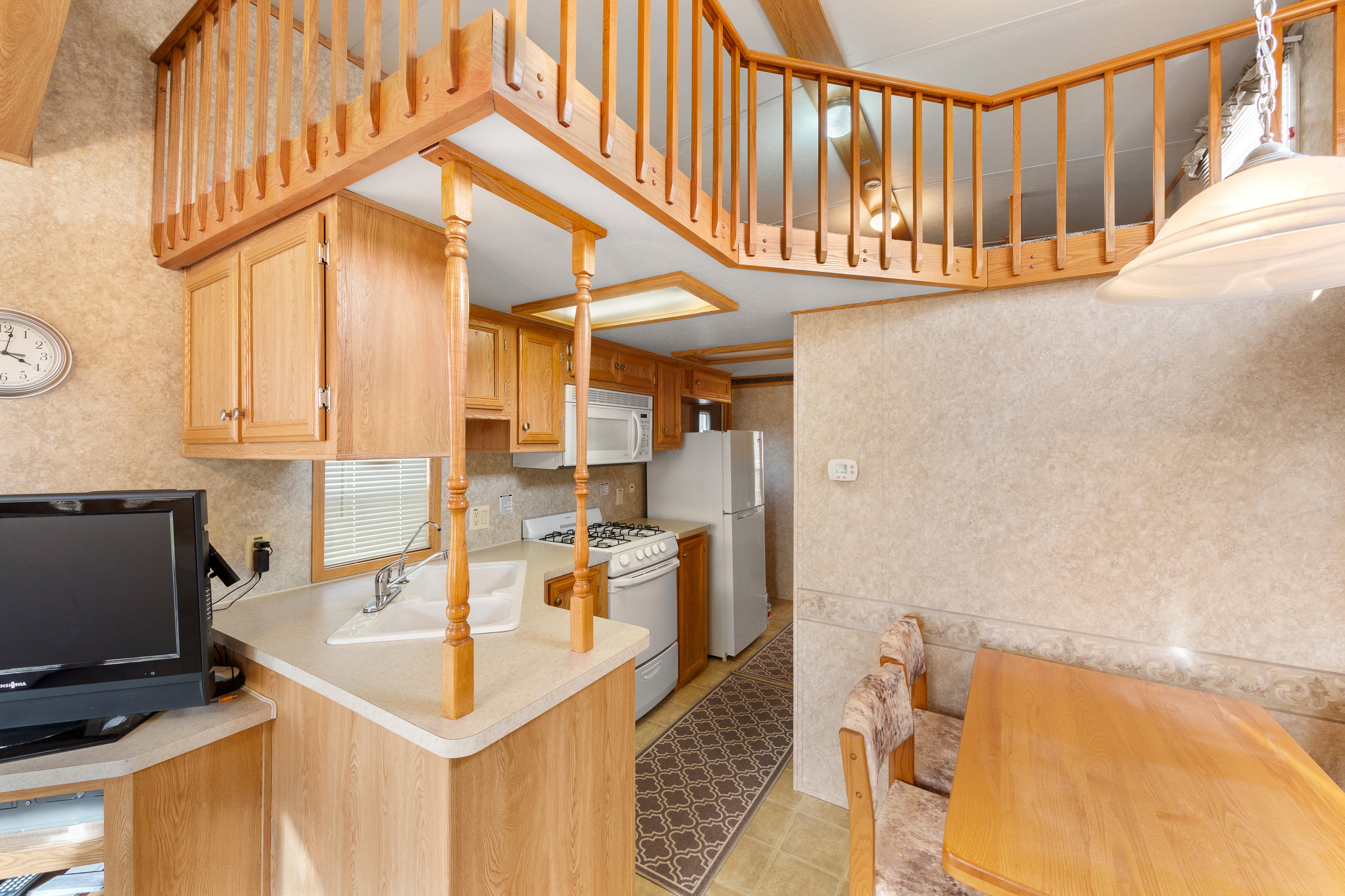 Kitchen featuring white appliances, light countertops, light brown cabinets, wallpapered walls, and a peninsula