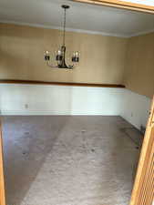Empty room with crown molding, carpet flooring, and a chandelier