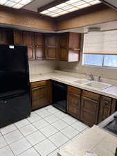 Kitchen with tile countertops, black appliances, dark brown cabinets, open shelves, and light tile patterned floors