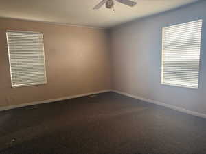 Unfurnished room with dark colored carpet and ceiling fan
