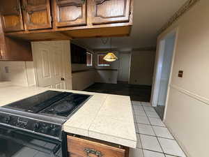 Kitchen featuring electric range, light countertops, a peninsula, hanging light fixtures, and light tile patterned floors