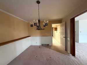 Unfurnished dining area with carpet flooring, a chandelier, and crown molding