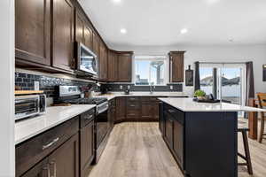 Kitchen with stainless steel appliances, dark brown cabinetry, a breakfast bar, light wood-style flooring, and decorative backsplash