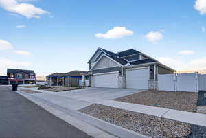 View of front facade featuring a gate, driveway, stone siding, board and batten siding, and an attached garage