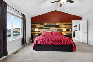 Carpeted bedroom with vaulted ceiling, an accent wall, ceiling fan, and wood walls