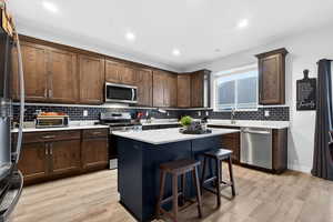 Kitchen featuring a breakfast bar area, stainless steel appliances, dark brown cabinets, light wood-style flooring, and recessed lighting