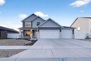 View of front of house featuring covered porch, stone siding, board and batten siding, driveway, and a garage