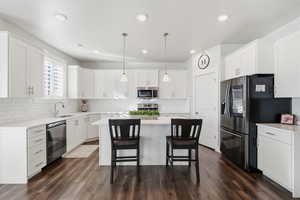 Kitchen featuring appliances with stainless steel finishes, decorative light fixtures, white cabinetry, a kitchen island, and dark wood-type flooring