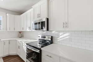 Kitchen featuring appliances with stainless steel finishes, white cabinets, dark wood-type flooring, decorative backsplash, and light stone countertops