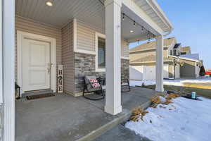 Snow covered property entrance with a porch and stone siding
