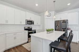 Kitchen featuring stainless steel appliances, a kitchen island, decorative light fixtures, a breakfast bar, and white cabinets