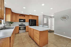 Kitchen featuring black appliances, light countertops, a kitchen island, recessed lighting, and brown cabinetry